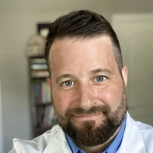 Dr. Kevin Bickart, wearing a white coat and blue shirt, smiling.