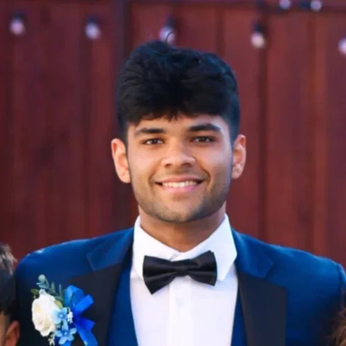 Rishit Bhat wearing formal dress, smiling in front of a red background.